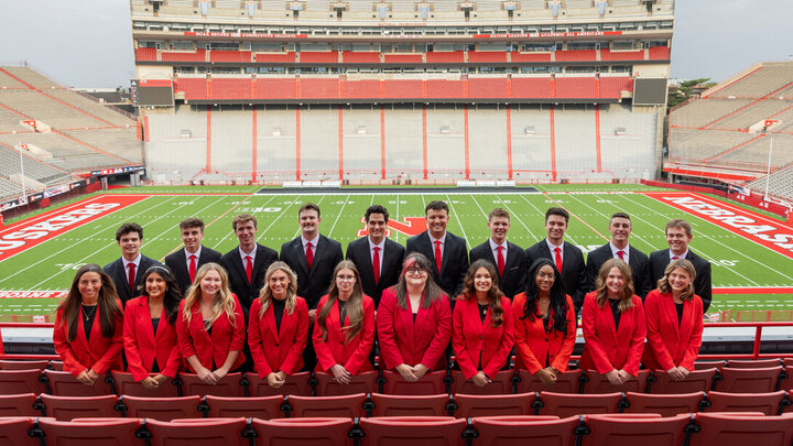 Ten young men and 10 young women — all 2025 homecoming royalty finalists — pose for a photo in the stands at Memorial Stadium, with the football field in the background. The men are wearing black suits with red ties, and the women are wearing red blazers with black shirts. Ten young men and 10 young women — all 2025 homecoming royalty finalists — pose for a photo in the stands at Memorial Stadium, with the football field in the background. The men are wearing black suits with red ties, and the women are wearing red blazers with black shirts.
